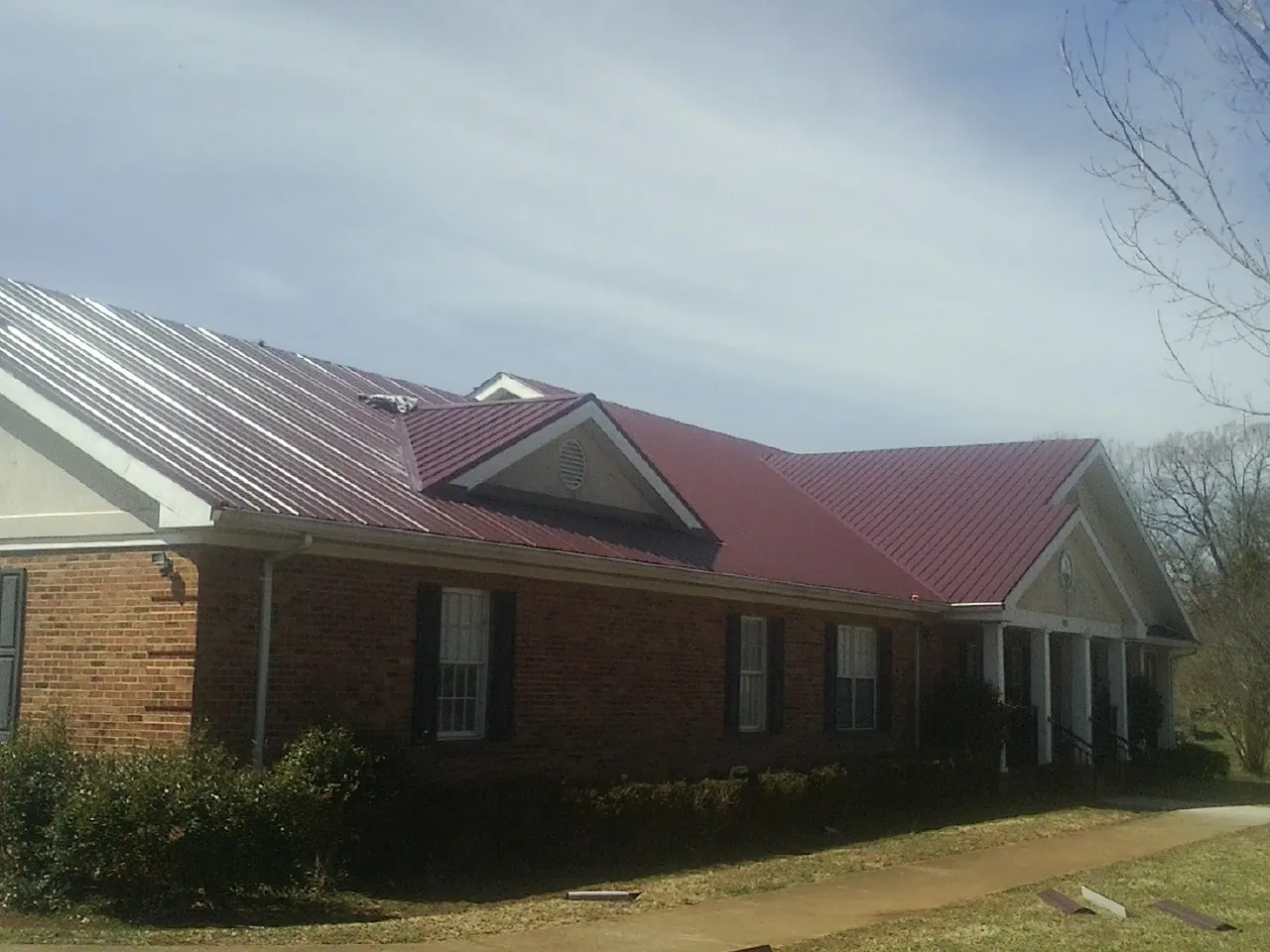Red metal roof with gabled entries on a long brick building, from a Hail Damage Roof Repair job in West Leyden