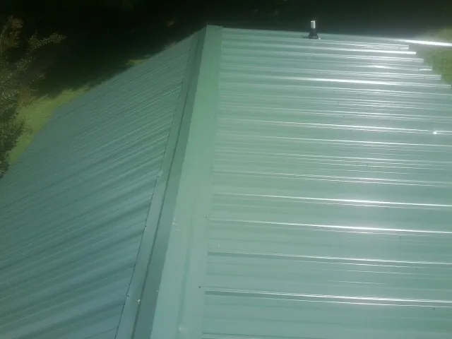 New green metal panels meeting at the ridge of a roof — Flat Roof Repair work by our crew in West Leyden