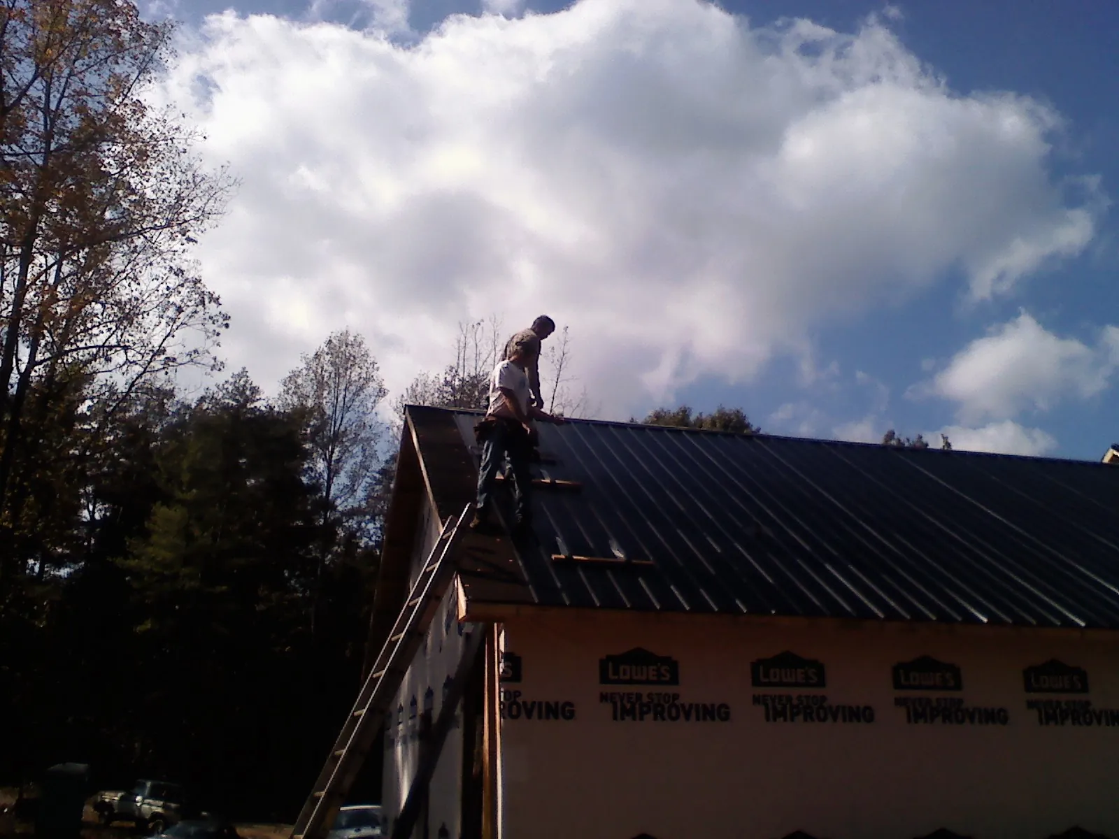 Roofer fastening dark metal panels high against a cloudy sky, from a Roof Inspection job in West Leyden