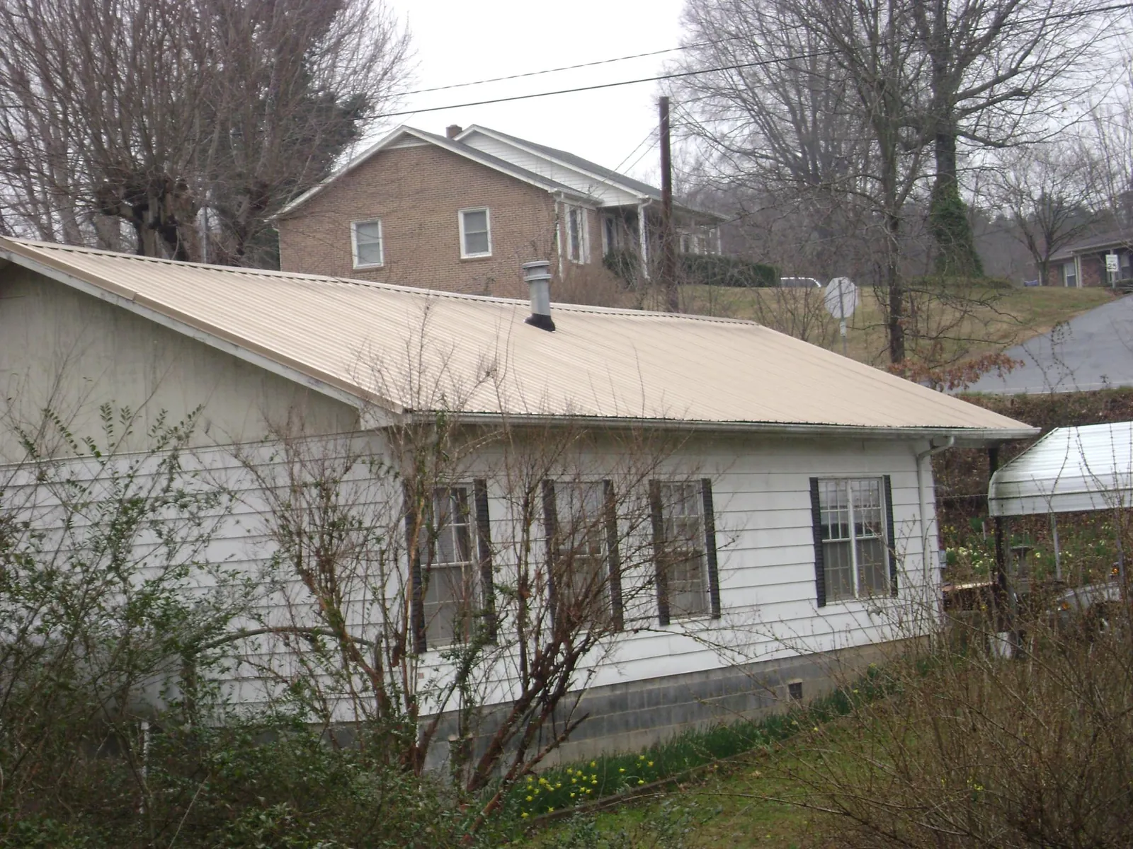 Tan metal roof on a white sided house set into a hillside — Commercial Roofing by Roofing Brothers in West Leyden