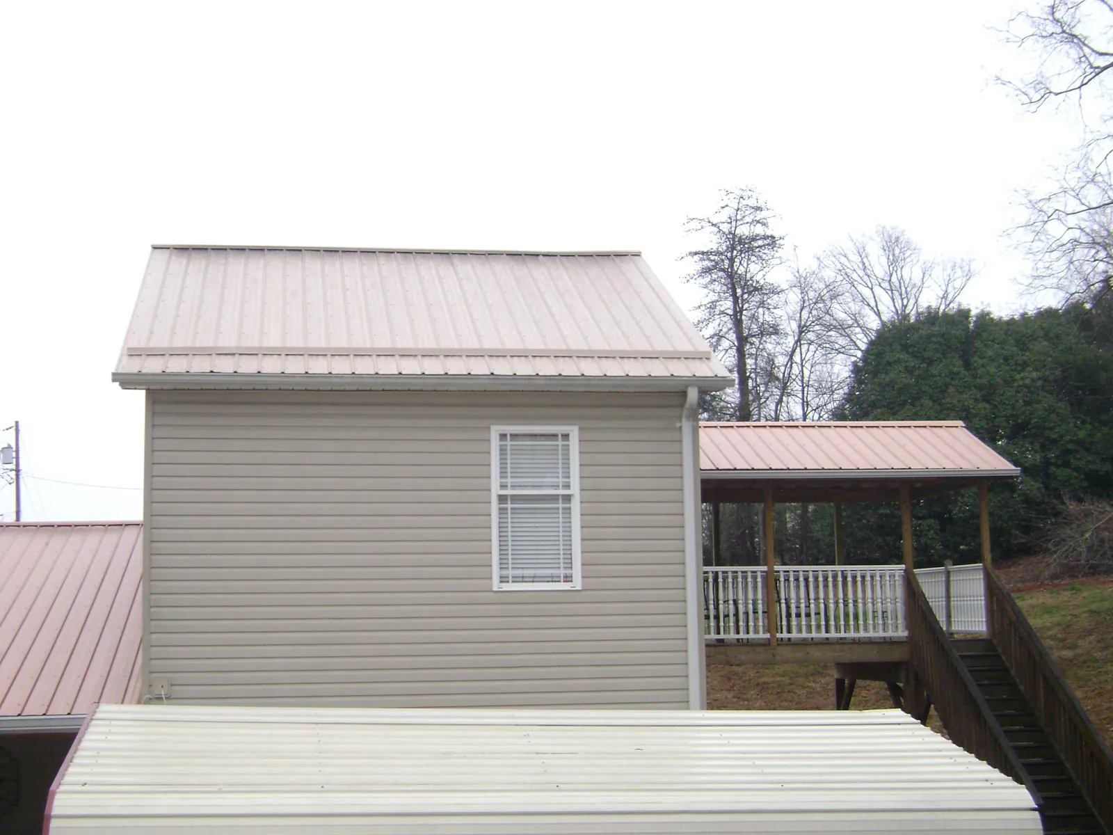 Tan metal roofs on a two story addition and attached porch, from a Roof Replacement job in West Leyden